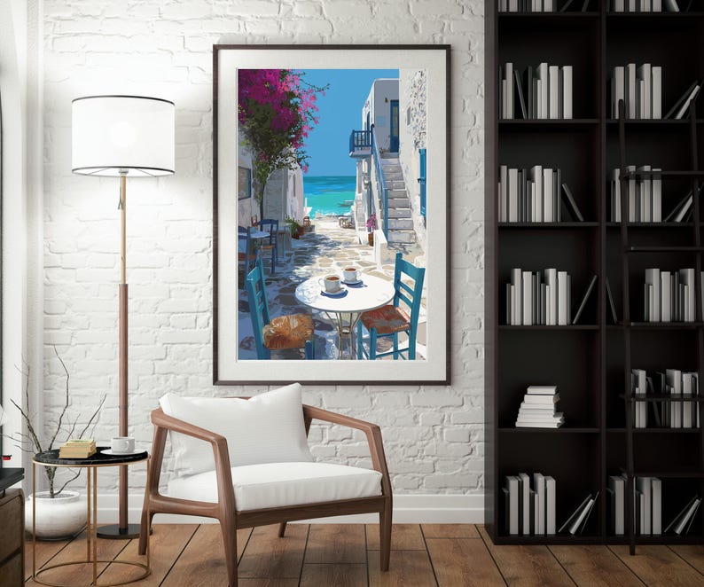 May include: Framed art print depicting a coastal scene with white buildings, blue accents, and a turquoise sea. A table with two cups of coffee and chairs are in the foreground. Pink flowers and a blue sky complete the scene.