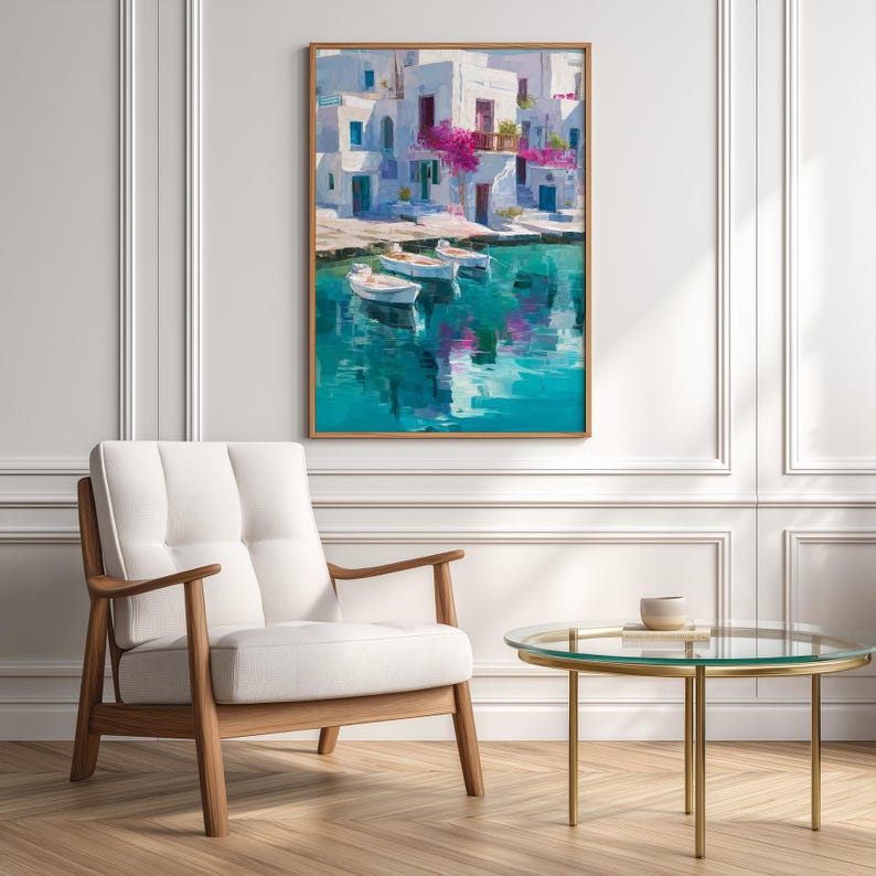 May include: A framed art print depicts a coastal scene with white buildings, blue doors, and vibrant pink flowers. Three small boats float on turquoise water, reflecting the buildings. The artwork is displayed above a white armchair and a round glass table.
