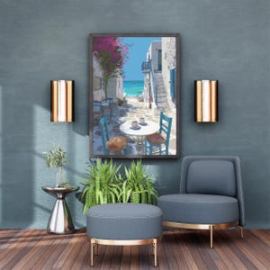 May include: A framed print depicts a coastal scene with white buildings, blue accents, and a vibrant pink flowering tree. The artwork hangs above a blue armchair, ottoman, and a small side table with greenery. Two wall sconces flank the artwork.