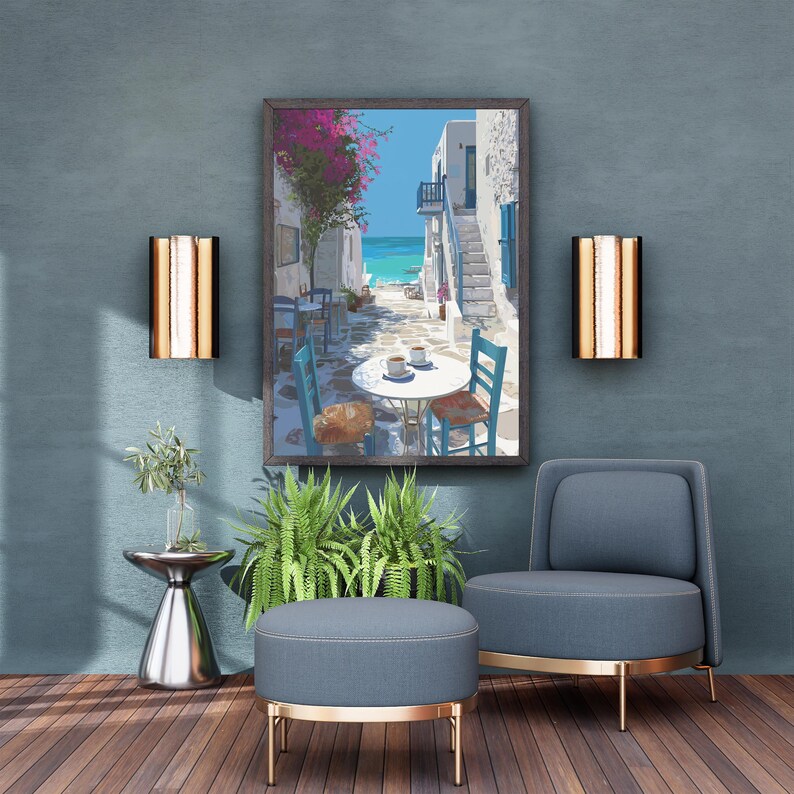 May include: A framed print depicts a coastal scene with white buildings, blue accents, and a vibrant pink flowering tree. The artwork hangs above a blue armchair, ottoman, and a small side table with greenery. Two wall sconces flank the artwork.