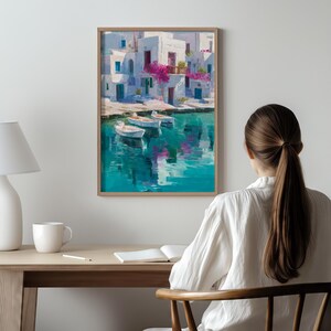 May include: A framed art print depicts a coastal scene with white buildings, blue doors, and vibrant pink flowers. Three small boats float on turquoise water, reflecting the buildings. The artwork is displayed on a wall.