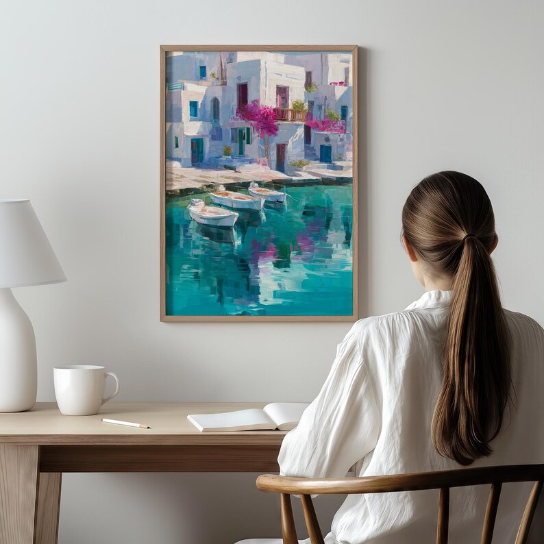 May include: A framed art print depicts a coastal scene with white buildings, blue doors, and vibrant pink flowers. Three small boats float on turquoise water, reflecting the buildings. The artwork is displayed on a wall.