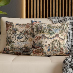 May include: Two decorative throw pillows with a tapestry design. The pillows feature scenes of children, a bicycle, and a house with an American flag. The color palette includes blue, red, green, and cream.