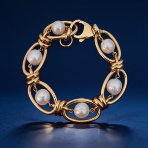 Könnte beinhalten: Ein goldfarbenes Gliederkettenarmband mit fünf runden weißen Perlen, die in den ovalen Metallgliedern hängen. Das Armband wird mit einem Karabinerverschluss geschlossen und zeichnet sich durch eine polierte Metalloberfläche und glatte Perlen aus.