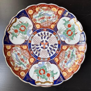 Può includere: Piatto decorativo in ceramica con bordo smerlato. Il piatto presenta un motivo floreale centrale ed è diviso in sezioni con motivi floreali e di uccelli in rosso, blu e oro. Il piatto ha un bordo dorato.