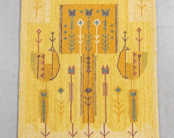May include: A woven wall hanging in shades of yellow, featuring a central rectangular design with floral and geometric patterns in orange, blue, and white. The piece has a textured surface and a small signature in the lower right corner.