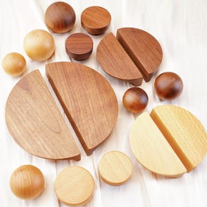Peut inclure: Une collection de boutons et poignées de meubles en bois de différentes formes et tailles. Les boutons sont sphériques, tandis que les poignées sont semi-circulaires. Les tons de bois varient du clair au brun foncé, créant une esthétique naturelle et chaleureuse.