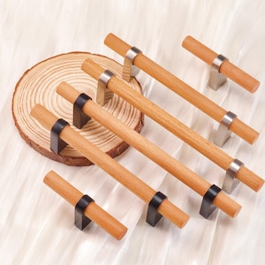 May include: Wooden cabinet pulls with a natural finish. The cylindrical pulls are mounted on metal brackets, some silver and some black. The pulls are arranged on a light-coloured surface. The image also shows a wooden slice.