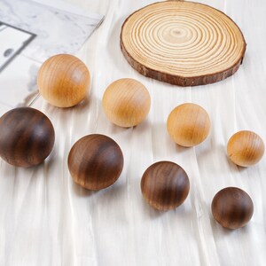 Puede incluir: Una colecci&oacute;n de esferas de madera en varios tama&ntilde;os y tonos de marr&oacute;n y beige. Tambi&eacute;n hay una rodaja de madera circular con anillos de crecimiento visibles. Las esferas est&aacute;n dispuestas sobre una superficie blanca texturizada.