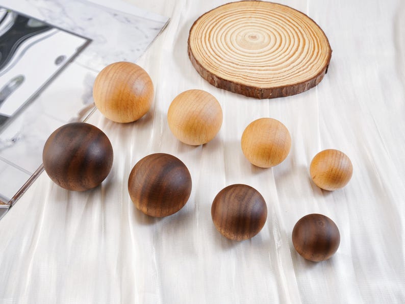 Puede incluir: Una colecci&oacute;n de esferas de madera en varios tama&ntilde;os y tonos de marr&oacute;n y beige. Tambi&eacute;n hay una rodaja de madera circular con anillos de crecimiento visibles. Las esferas est&aacute;n dispuestas sobre una superficie blanca texturizada.