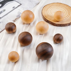 Puede incluir: Una colecci&oacute;n de esferas de madera en varios tama&ntilde;os y tonos de marr&oacute;n y beige. Algunas esferas son de color beige claro, mientras que otras son de un marr&oacute;n m&aacute;s oscuro. Tambi&eacute;n hay una peque&ntilde;a rodaja de madera con una esfera encima.