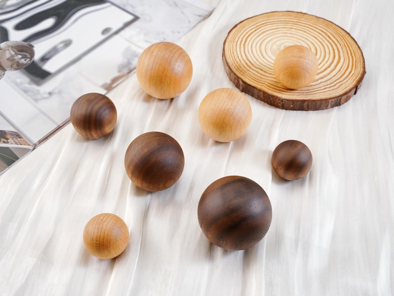 Puede incluir: Una colecci&oacute;n de esferas de madera en varios tama&ntilde;os y tonos de marr&oacute;n y beige. Algunas esferas son de color beige claro, mientras que otras son de un marr&oacute;n m&aacute;s oscuro. Tambi&eacute;n hay una peque&ntilde;a rodaja de madera con una esfera encima.