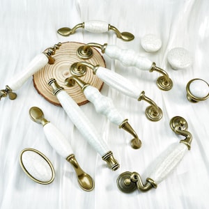 Peut inclure: Divers poignées et boutons de meubles en céramique blanche et laiton. Les poignées présentent différents designs, avec des détails en laiton et des sections en céramique blanche. Les boutons sont ronds et ovales, avec une finition assortie en céramique blanche et laiton.