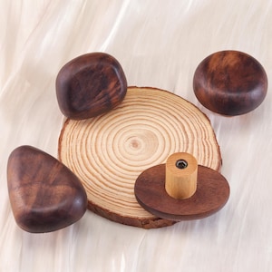 Może przedstawiać: Kolekcja drewnianych przedmiot&oacute;w, w tym okrągły plaster drewna, kilka gładkich, ciemnobrązowych drewnianych kształt&oacute;w i mały drewniany korek do butelki. Obiekty są ułożone na jasnej, teksturowanej powierzchni.