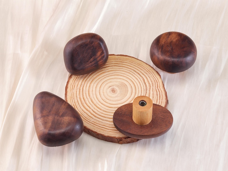 Może przedstawiać: Kolekcja drewnianych przedmiot&oacute;w, w tym okrągły plaster drewna, kilka gładkich, ciemnobrązowych drewnianych kształt&oacute;w i mały drewniany korek do butelki. Obiekty są ułożone na jasnej, teksturowanej powierzchni.