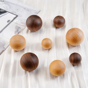 Puede incluir: Una colecci&oacute;n de esferas de madera en varios tama&ntilde;os y tonos de marr&oacute;n y beige. Las esferas est&aacute;n dispuestas sobre una superficie blanca texturizada, algunas parecen ser de madera te&ntilde;ida m&aacute;s oscura. La veta natural de la madera es visible.