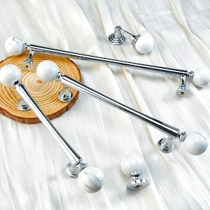 May include: A collection of polished chrome curtain rods with white marble-like sphere finials. The rods are displayed on a white fabric background, with a wooden slice in the center. The hardware is designed for window treatments.