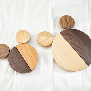 May include: Wooden coasters in various sizes and wood tones. Two larger coasters are split diagonally, with one half a lighter wood and the other a darker wood. Smaller, round coasters are also visible.