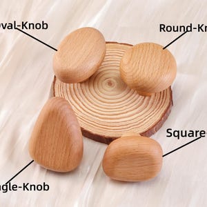 Może przedstawiać: Cztery drewniane gałki do szafek o r&oacute;żnych kształtach: owalnym, okrągłym, tr&oacute;jkątnym i kwadratowym. Gałki są jasnobrązowe i leżą na drewnianym plastrze. Etykiety tekstowe identyfikują każdy kształt gałki.