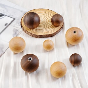 Puede incluir: Una colecci&oacute;n de esferas de madera en varios tama&ntilde;os y tonos de marr&oacute;n y beige. Algunas esferas tienen un agujero perforado. Las esferas est&aacute;n dispuestas sobre una tela blanca y una rodaja de madera.