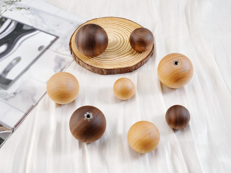 Puede incluir: Una colecci&oacute;n de esferas de madera en varios tama&ntilde;os y tonos de marr&oacute;n y beige. Algunas esferas tienen un agujero perforado. Las esferas est&aacute;n dispuestas sobre una tela blanca y una rodaja de madera.