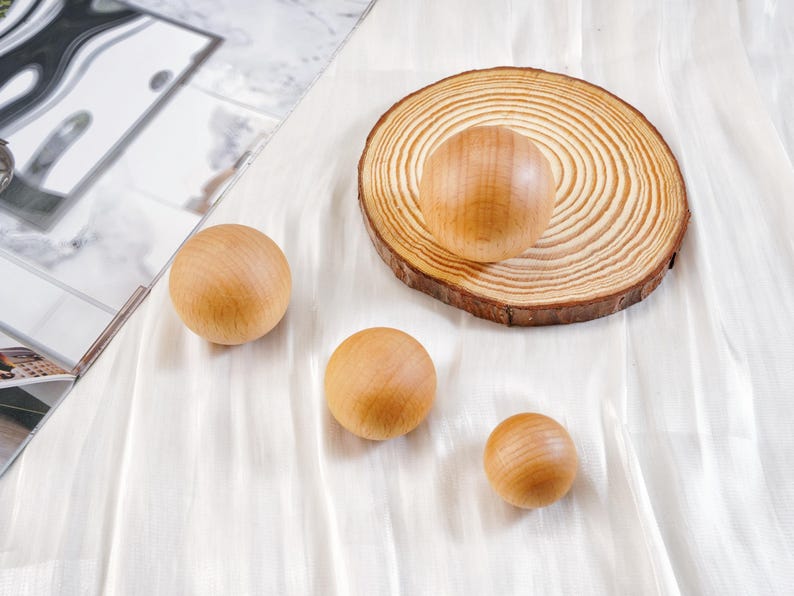 Puede incluir: Varias esferas de madera de diferentes tama&ntilde;os, junto con una rodaja de madera con una esfera encima. Las esferas y la rodaja son de color marr&oacute;n claro, con la veta de la madera visible. Est&aacute;n dispuestas sobre una superficie blanca y texturizada.