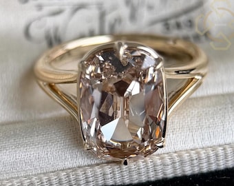 May include: A gold ring featuring a large, rectangular, champagne-colored faceted gemstone held by four prongs. The band has a split-shank design that tapers toward the center stone, creating a polished and reflective appearance on the metal surface.