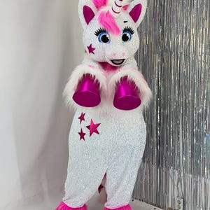 Könnte beinhalten: Ein weißes, paillettenbesetztes Einhornkostüm mit rosa Mähne, Horn und Akzenten. Das Kostüm hat rosa Hufe, Ohren und Sterndetails. Das Einhorn hat blaue Augen und eine flauschige weiße Brust. Das Kostüm ist zum Tragen bestimmt.