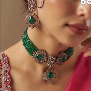 Peut inclure: Un ensemble de bijoux orné comprenant un collier et des boucles d'oreilles. Le collier est composé de plusieurs rangées de perles vertes et de pendentifs décoratifs avec des pierres de couleur émeraude. Les boucles d'oreilles reprennent le design du collier.