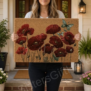 May include: A rectangular coir doormat featuring a printed design of vibrant red poppy flowers on long green stems. Two light blue butterflies are positioned in the upper right corner of the mat, adding a delicate detail to the floral scene.