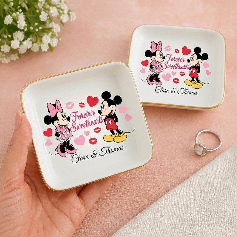 May include: Two white square ring dishes with gold trim, featuring Mickey and Minnie Mouse illustrations. The dishes have the text "Forever Sweethearts" and the names "Clara & Thomas" printed on them, along with hearts and lip prints.