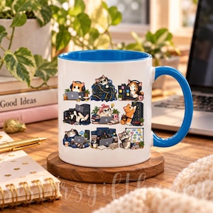 May include: A white ceramic mug with a bright blue interior and handle, featuring a repeating graphic print of cartoon cats working on computers, managing cables, and organizing office tasks in various colorful, detailed desk settings.