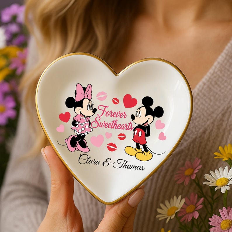 May include: Heart-shaped trinket dish with a gold rim, featuring Mickey and Minnie Mouse. The dish is white with pink hearts, lips, and the words "Forever Sweethearts." The names "Clara & Thomas" are also printed on the dish.