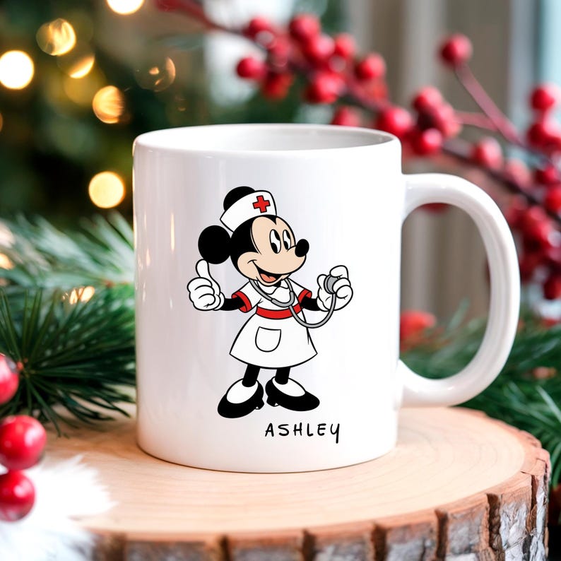 Peut inclure: Mug en c&eacute;ramique blanche avec un dessin de souris infirmi&egrave;re. La souris porte un uniforme et un bonnet d'infirmi&egrave;re, tenant un st&eacute;thoscope. Le mug porte le nom "ASHLEY". Le mug est blanc avec une anse incurv&eacute;e.