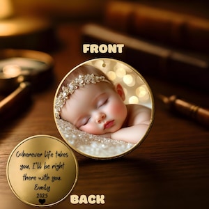 May include: A gold-colored, round pendant with a baby's photo on the front. The baby is sleeping and wearing a jeweled headband. The back of the pendant has the text: "Wherever life takes you, I'll be right there with you. Emily 2025."