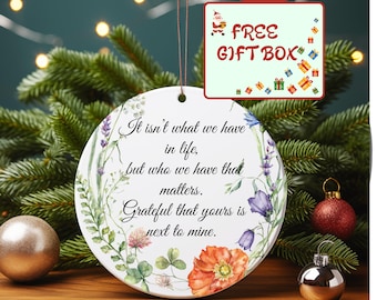 May include: A round white ceramic ornament featuring a floral design with lavender, poppies, and clover. The text reads: It isn't what we have in life, but who we have that matters. Grateful that yours is next to mine. It hangs from a thin string.