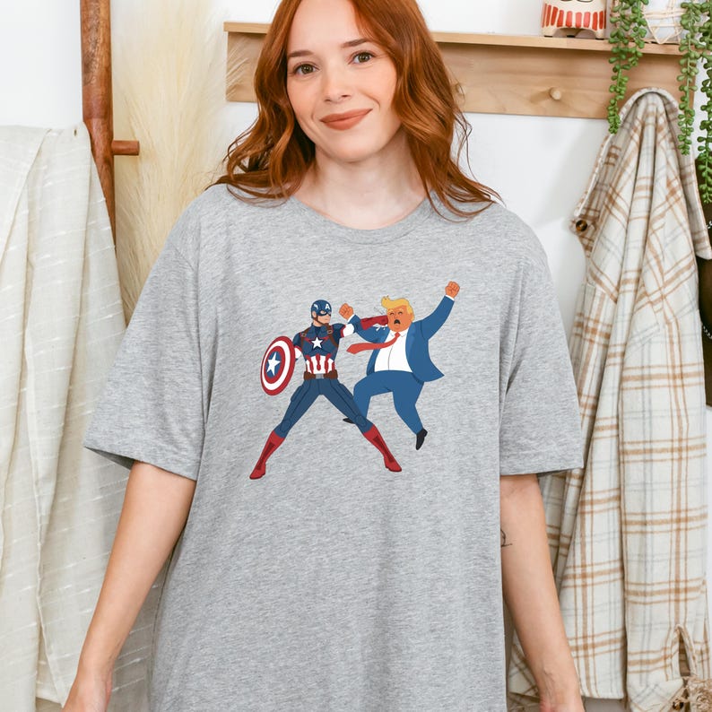 May include: A light grey t-shirt with a graphic of Captain America punching a man in a blue suit. Captain America is in his costume and holding his shield. The man in the suit has blonde hair and a red tie.