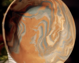 Puede incluir: Un cuenco de cerámica con un diseño veteado único. El cuenco presenta patrones arremolinados de colores naranja, azul y crema. El cuenco hecho a mano es una pieza decorativa para el hogar.