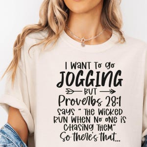 May include: Cream-colored t-shirt with the text "I WANT To go JOGGING BUT Proverbs 28:1 says 'THE WICKED RUN WHEN No ONE IS CHASING THEM' So there's that..." in black script.