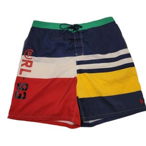 May include: Color-blocked swim trunks in red, white, navy, and yellow. The trunks feature the text "RL 93" in black on the left leg and a small red logo on the right leg. The waistband is green with a drawstring.