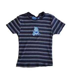 May include: Navy blue and white striped t-shirt featuring an embroidered Care Bear design on the front. The t-shirt has short sleeves and a ribbed texture. The Care Bear logo is visible on the neckline.