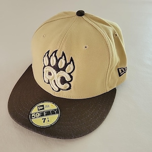 May include: Tan and brown baseball cap with a flat brim. The cap features a paw print logo with the letters "RC" in white. The cap size is 7 1/4 (57.7cm). A New Era logo is visible on the side.