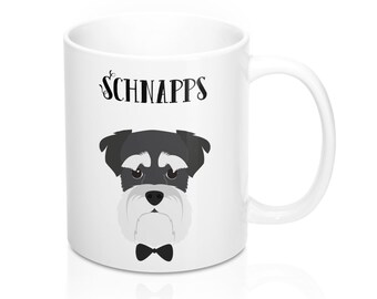 May include: White ceramic mug featuring a Schnauzer dog illustration with a black bow tie. The mug has the word "SCHNAPPS" in black script above the dog's head. The dog has black and gray fur and a white beard.