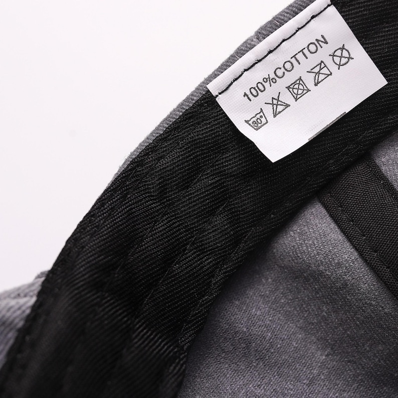 May include: Close-up of a gray baseball cap's interior, showcasing a black sweatband and a white tag. The tag reads "100% COTTON" with care symbols. The cap's fabric appears textured, with visible stitching.