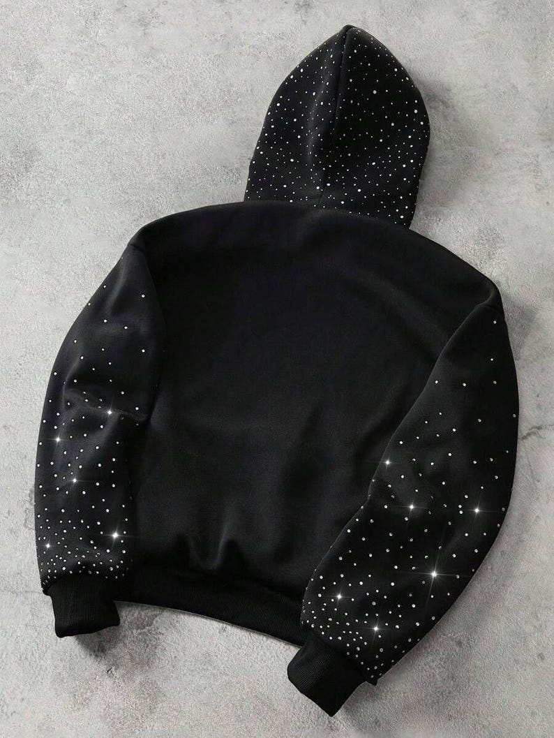 May include: Black hoodie with a hood and long sleeves. The hood and sleeves are embellished with sparkling, scattered rhinestones. The cuffs and hem are solid black.