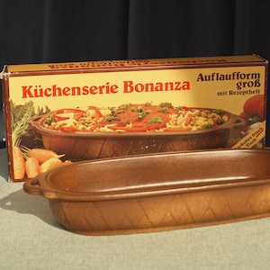 May include: Brown ceramic baking dish with a diamond pattern on the sides. A box behind it reads "Küchenserie Bonanza" and shows a picture of a casserole dish. The box also says "Auflaufform groß mit Rezeptheft".