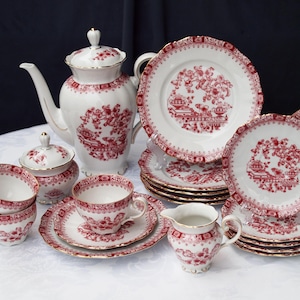 Könnte beinhalten: Ein komplettes Vintage-Teeservice in Weiß mit rotem Blumen- und Landschaftsmuster. Das Set beinhaltet eine Teekanne, eine Zuckerdose, einen Sahnekännchen, Tassen, Untertassen und Teller. Die Ränder sind goldfarben.