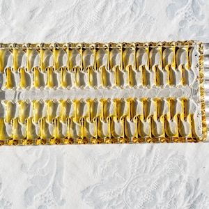 May include: A rectangular glass serving tray with a repeating pattern of yellow and clear glass elements. The tray has a textured, decorative border and is set against a white, patterned surface.