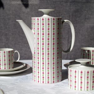 May include: A white porcelain coffee set with a floral pattern. The set includes a tall coffee pot, sugar bowl, two cups, and saucers. The pattern features vertical stripes with pink and green floral accents.