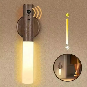 May include: A wall-mounted light fitting featuring a dark wood cylindrical body with a motion sensor at the top and a frosted white glass tube at the bottom emitting a warm glow. A vertical brightness slider icon is displayed to the right.